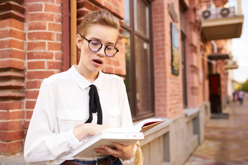 Женщина читает книгу на улице возле кирпичного здания