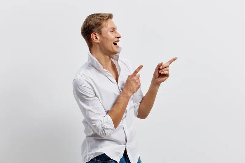smiling young caucasian man wearing white shirt pointing sideways looking excited happiness digital nomad concept studio portrait on white background