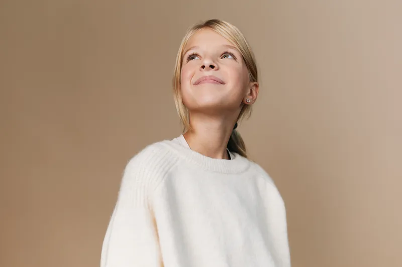 Authentic portrait of a young girl in a cozy sweater, capturing a candid moment of curiosity and playfulness for lifestyle and school themed photography.