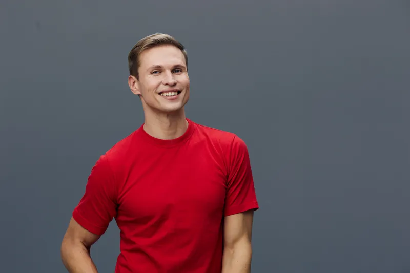 Smiling happy young caucasian man wearing red t-shirt looking camera standing against gray background digital nomad remote work concept