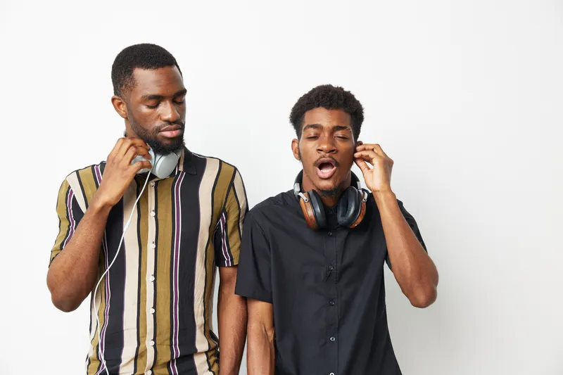 Two black men enjoying music together, showcasing friendship, laughter, and relaxed vibes. Perfect for themes of joy and connection through music.