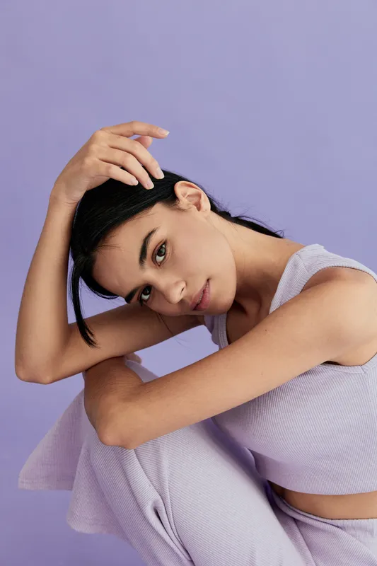 Young woman posing thoughtfully wearing lavender outfit against soft purple background, showcasing natural beauty and calm expression in stylish casual attire.