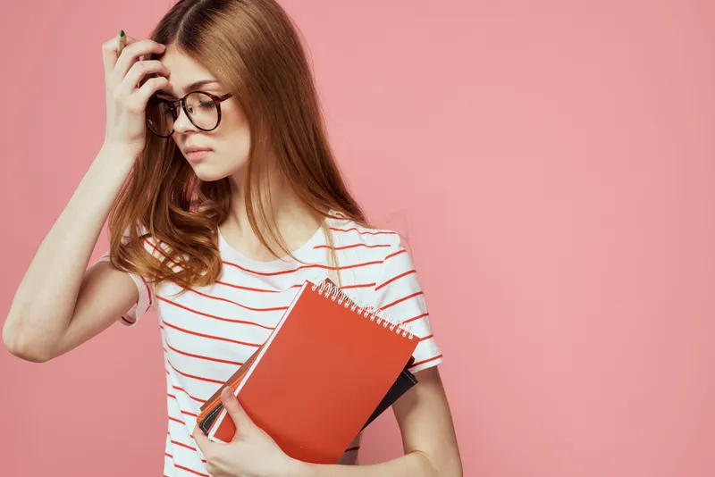 Молодая студентка с книгами на розовом фоне, в очках