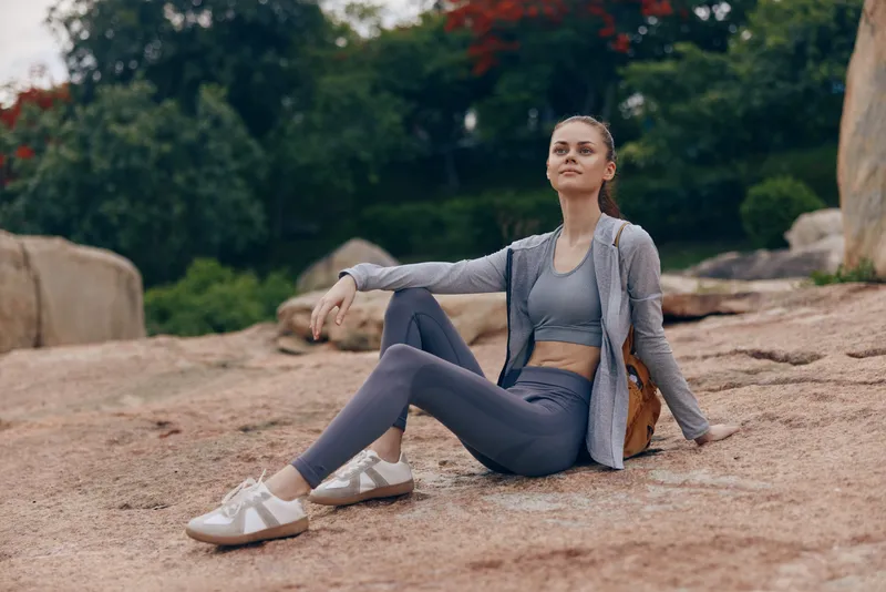 Young woman in athletic wear sitting on rock outdoors, portraying confidence and relaxation in nature, ideal for healthy lifestyle and fitness concepts
