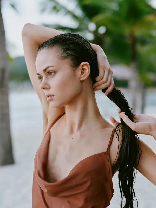 Portrait of a thoughtful woman on a beach, hair tied back, wearing a rust dress, with soft sunlight highlighting contours and a calm, contemplative mood.