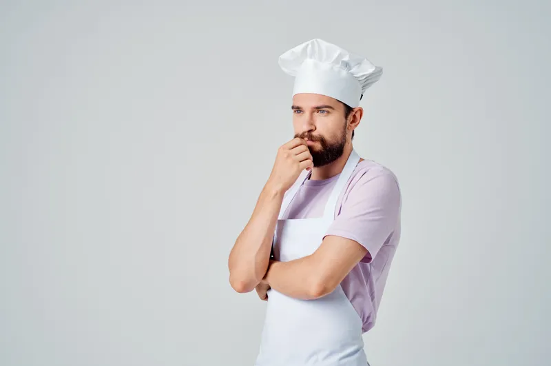 Бородатый шеф-повар мужского пола в белом фартуке на кухне ресторана с кухонной утварью