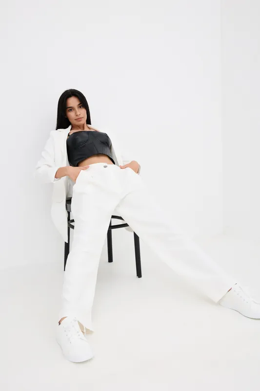 young woman in white pants and black top reclining on chair, casual outfit, minimalist indoor setting, relaxed pose, modern fashion style