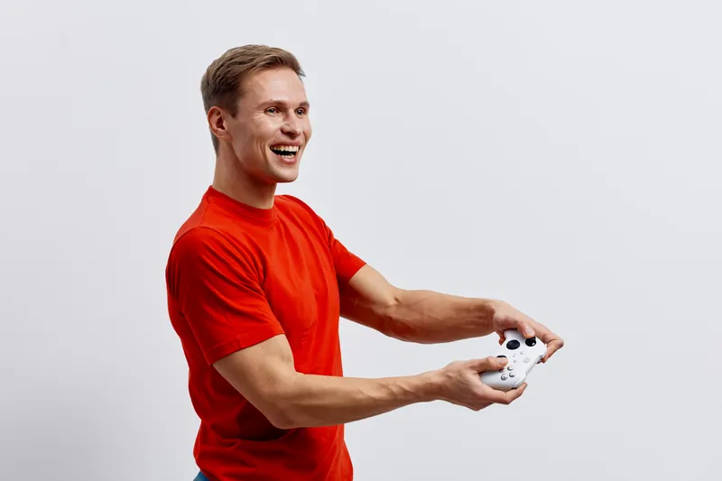 Young smiling man in red t-shirt holding a white drone with remote control in hands indoor studio shot happy expression casual style bright background. People lifestyle concept