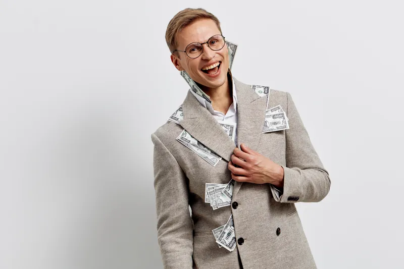 Smiling woman wearing glasses and beige blazer with torn banknotes pinned on it, cheerful and confident, standing against plain white wall, studio portrait. People lifestyle concept