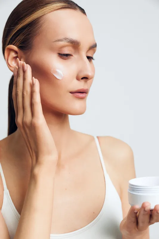 Woman in closeup applies skincare cream from a jar beside her face, facial selfcare for beauty, hydration, routine, smooth glow on skin, calm relaxation in spa style