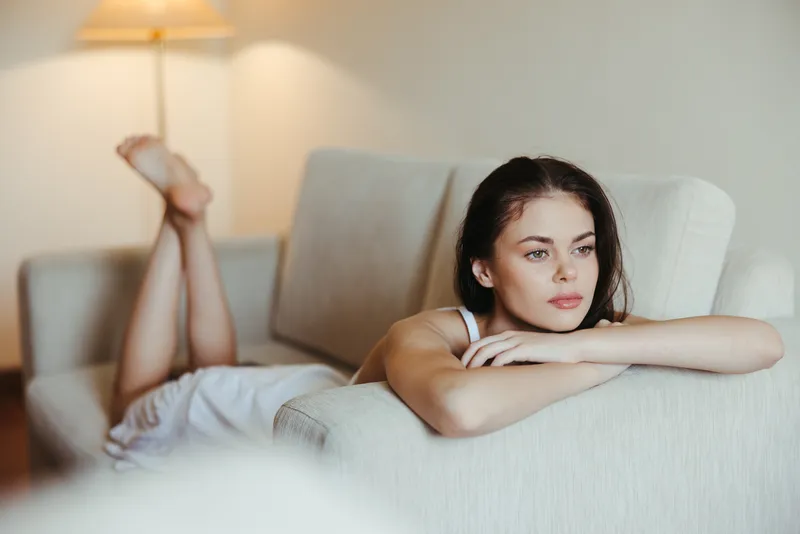 Счастливая девушка улыбается, лежа на диване дома, отдыхает в домашней обстановке, чувствуя комфорт и наслаждаясь солнечным светом