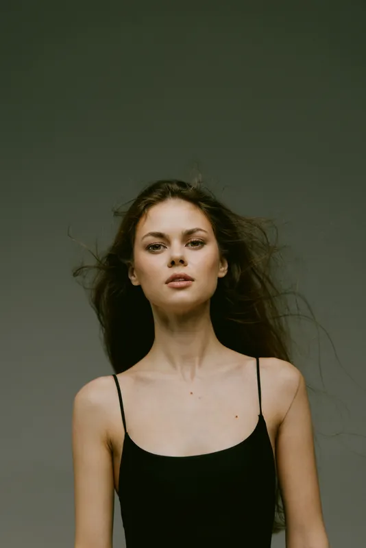 Portrait of a young woman with long hair wearing a black dress against a plain background.