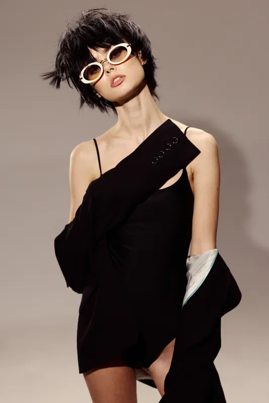 Stylish woman wearing black dress and sunglasses with confident pose in minimalistic setting, modern fashion look
