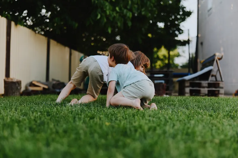 Two playful children crawling on green grass in a sunny backyard, enjoying the warmth of summer while engaging in imaginative play and exploration.
