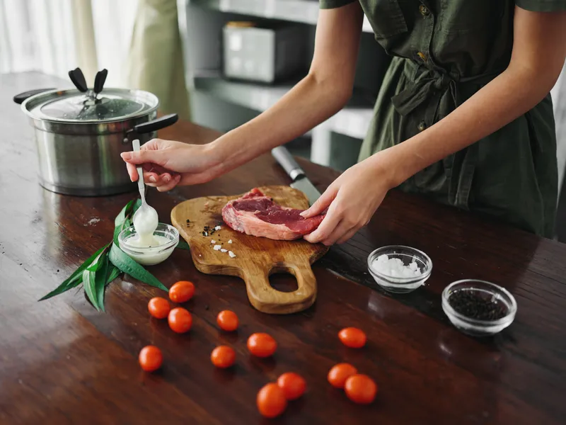 Женщина на кухне готовит ужин из мяса, овощей и специй на деревянном столе на фоне стильной кухни, крупный план рук, образ жизни