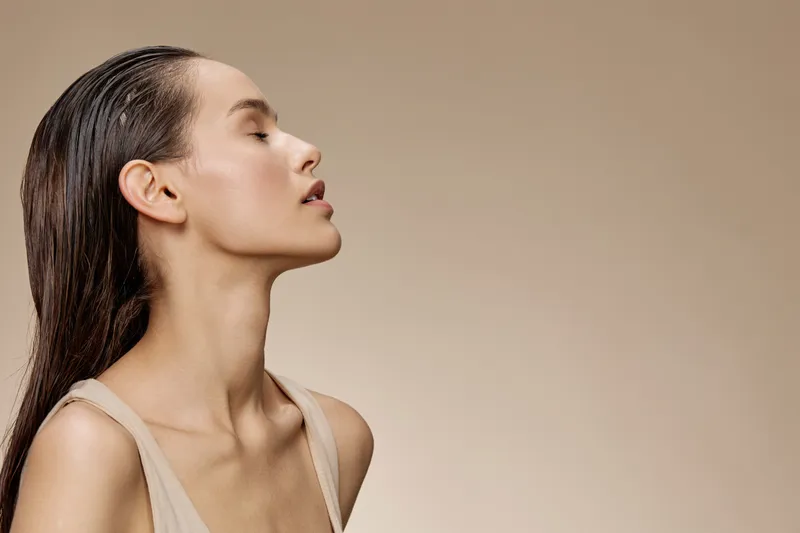 Elegant woman with long hair in neutral tones, showcasing a serene expression against a soft beige background, ideal for beauty and wellness concepts