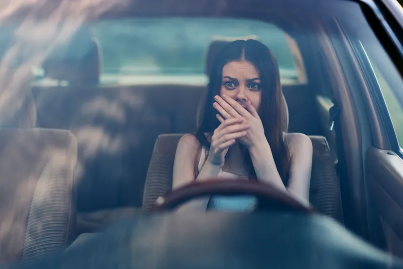 Young woman with fear expression covering mouth in car, showing anxiety, emotional distress, and concern in a blurred background setting.