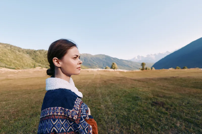 Woman portrait in expansive landscape with distant mountains and open field outdoors, thoughtful profile looking to horizon, travel scene with calm nature and soft sunlight.