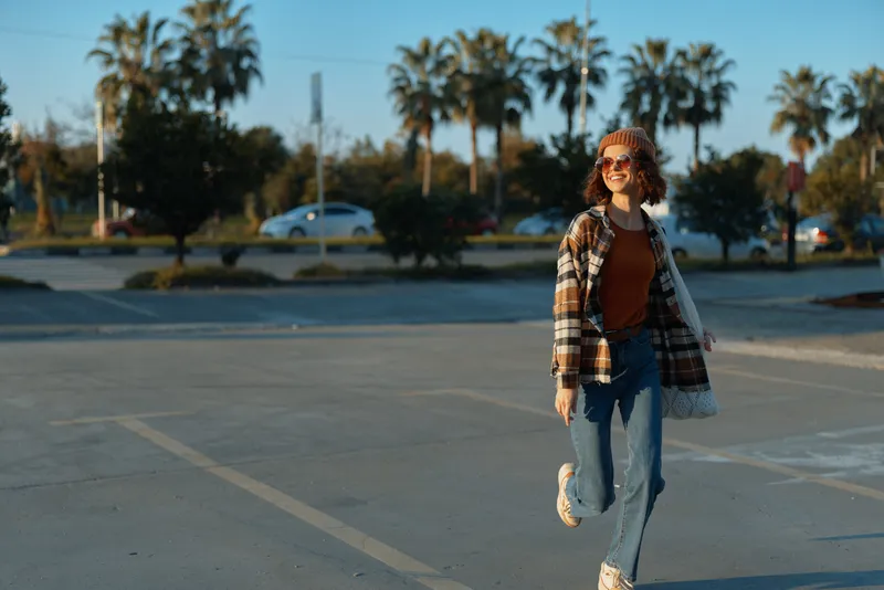 woman walking smile casual plaid sunglasses beanie sunset portrait of a young woman strolling in golden hour glow, candid lifestyle authenticity, emotional storytelling and mindful living in urban