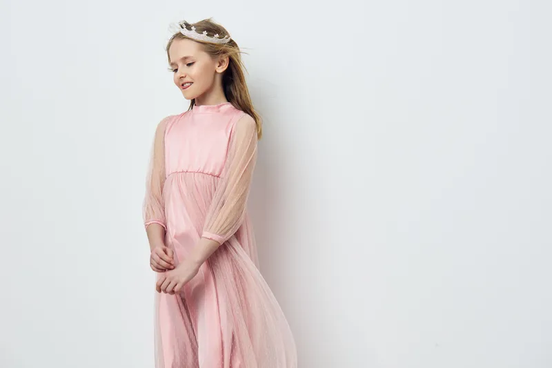 A young girl in a delicate pink dress, exuding joy and innocence, stands against a clean white background, perfect for showcasing childhood beauty