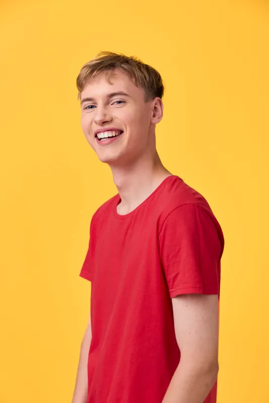 Smiling man in a red shirt stands against a bright yellow backdrop, conveying casual joy, warmth and optimism. Studio shot with strong color contrast and clean composition, ideal for lifestyle,