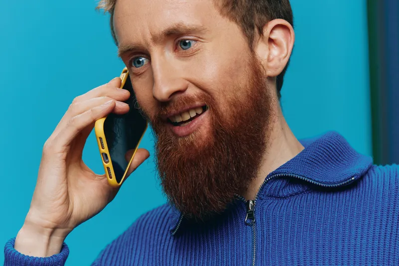 Портрет мужчины с телефоном в руках: он смотрит на экран и разговаривает по телефону на синем фоне