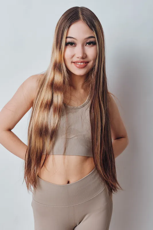Young woman with long hair and smile wearing sporty outfit posing confidently in front of white background with hands on hips for fitness and lifestyle.