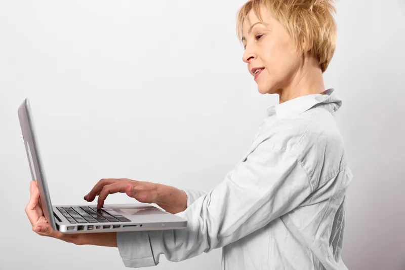 Profile woman typing on laptop for remote office work, communication and technology in an online workflow, bright white studio, soft light, focused expression