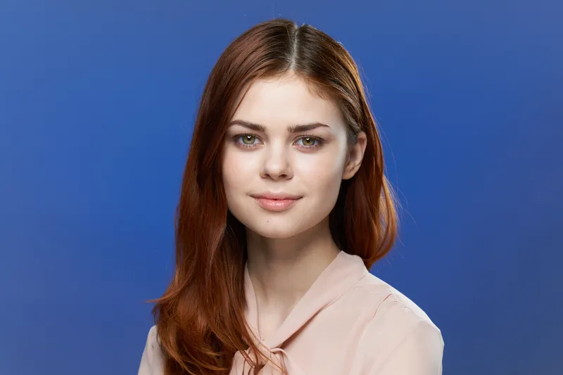 Симпатичная женщина в розовой рубашке, привлекательный взгляд, улыбка, синий фон, модель
