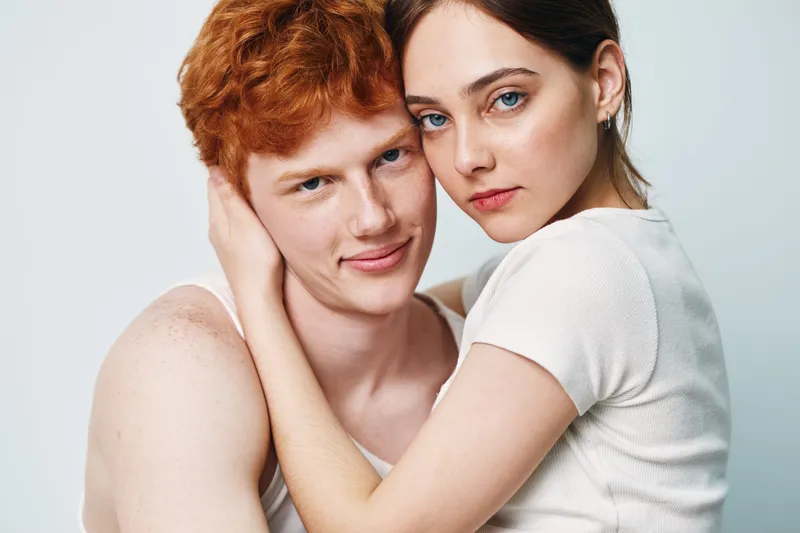 Couple, young man and woman in close embrace with affectionate expression on white background. Intimate portrait of lovers, relationship, love and connection with casual clothing.