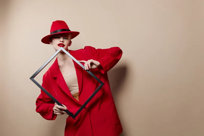 Симпатичная женщина с рамкой в руках в красной шляпе и куртке на изолированном фоне
