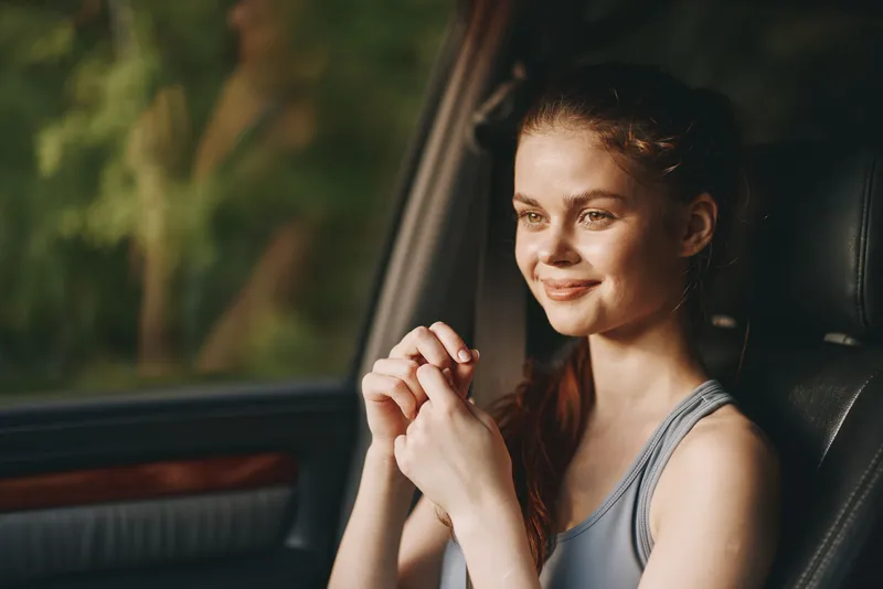 Happy young woman in sportswear smiling while sitting in a car, with natural background reflecting joy and relaxation in a warm color palette