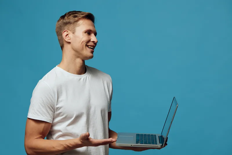 Smiling man holding laptop looking side standing isolated on blue background casual wear digital nomad technology freelance communication concept