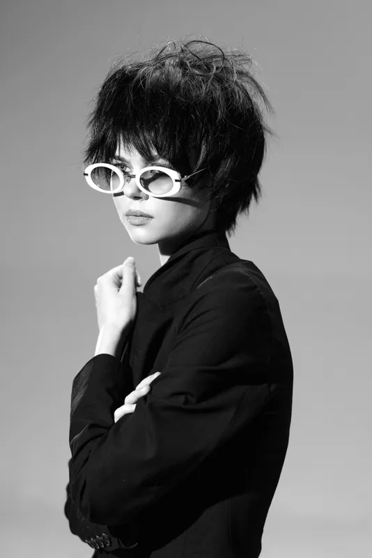 Stylish woman wearing white sunglasses in black and white portrait with edgy hairstyle and confident pose