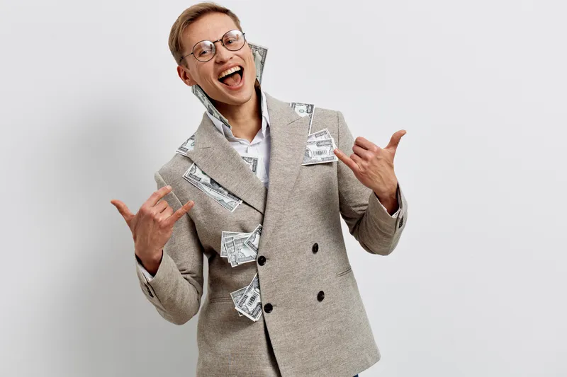 Joyful smiling man wearing smart casual suit with torn paper pieces, expressive cheerful mood, glasses, light background, studio portrait, lifestyle concept, human emotion