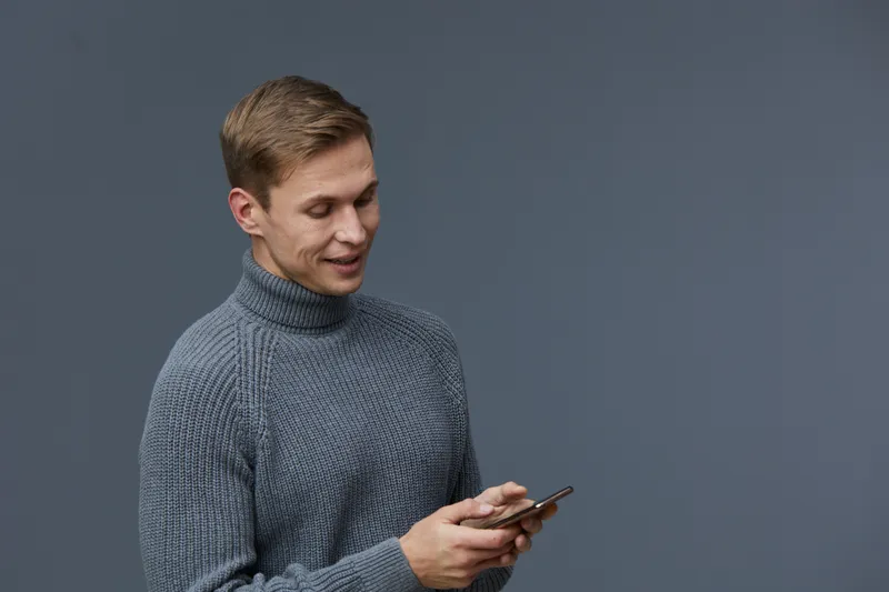 young man using phone smiling casual wear gray knitted sweater isolated on dark background digital nomad communication concept