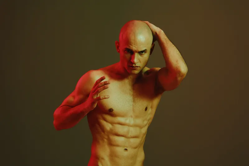 Athletic man posing confidently against a gradient background, conveying strength and determination. The image features dramatic lighting and artistic shadows.