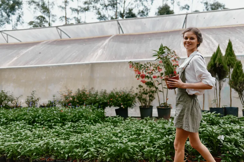 Smiling woman planting a small tree in a greenhouse, showcasing a healthy lifestyle and connection to nature with vibrant green plants