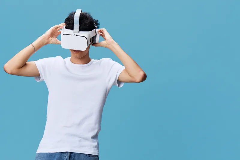 young man wearing white t-shirt using virtual reality headset on blue background, immersive technology experience with casual style and modern gadget
