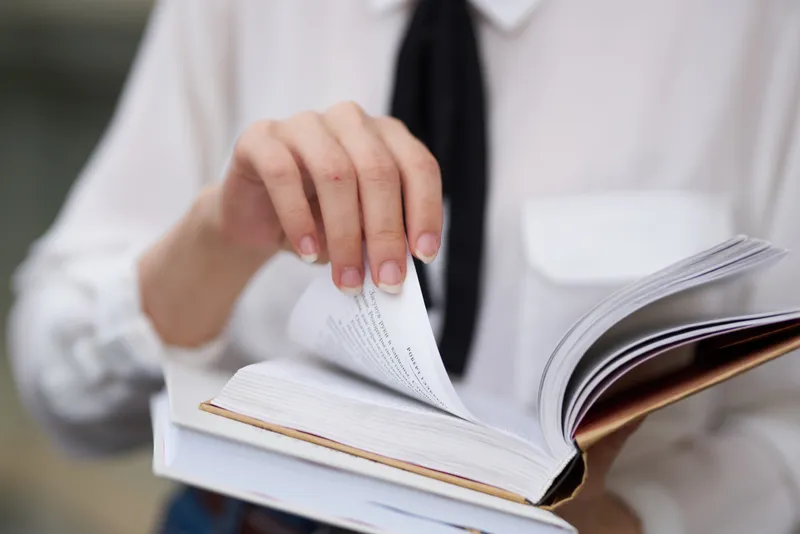 Студент в очках прогуливается по городу с книгой в руках, что символизирует образование