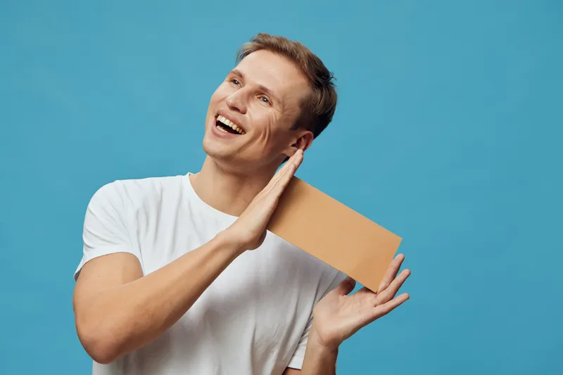 Smiling happy young caucasian man hold cardboard isolated on blue background digital detox lifestyle concept with casual white t-shirt bright mood studio portrait