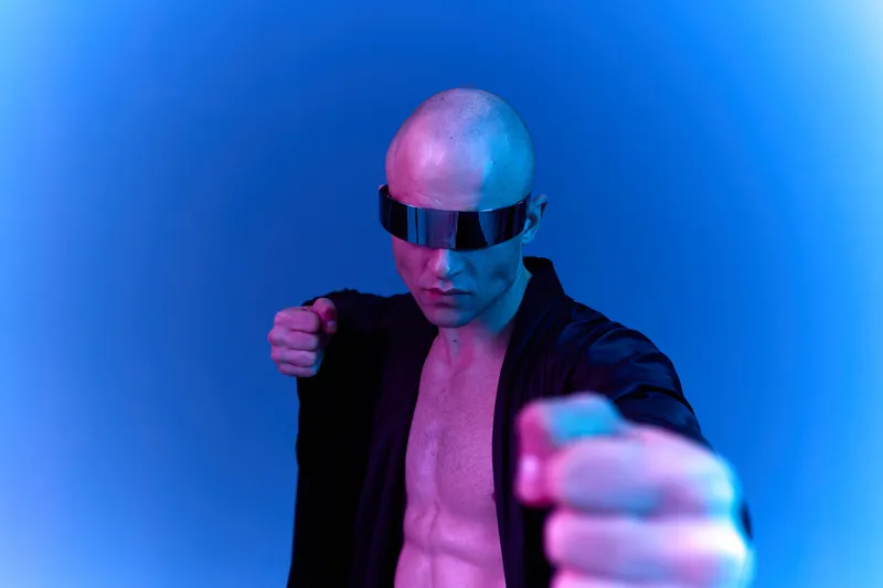 Intense man in futuristic glasses poses confidently against a vibrant gradient background, showcasing a bold and dynamic style. A striking representation of strength.