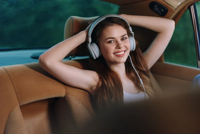 Young woman enjoying music with headphones in a car, relaxed and happy expression, soft background colors, ideal for lifestyle and music themes.