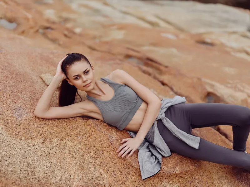 Fit young woman in athletic clothing lounging on rocks, showcasing a healthy lifestyle, confidence, and serenity in nature