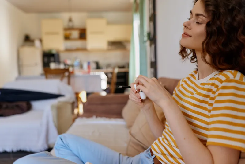 Cheerful woman indoors, relaxed at home, wearing a striped shirt, soft natural light, comfortable surroundings, everyday moment, candid lifestyle, cozy atmosphere, calm vibe