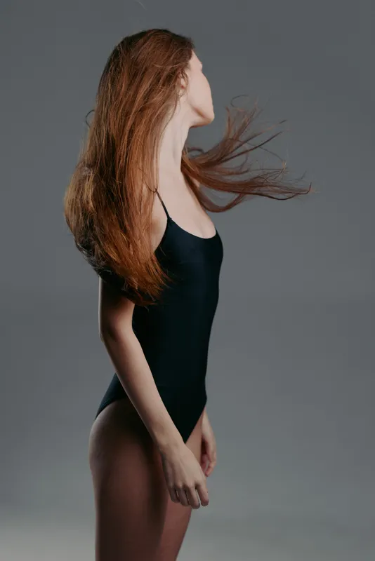 Woman with long red hair wearing black bodysuit against gray background, stylish and elegant look