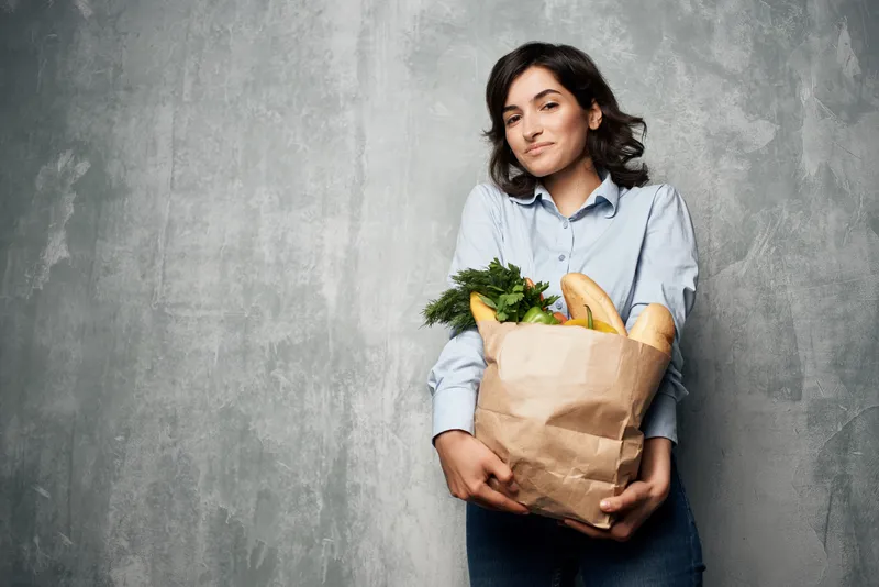 Женщина с пакетом продуктов покупает овощи