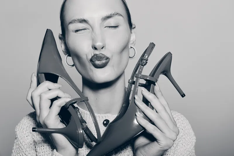 White woman with fair skin holding red high heels near her face, lips puckered as if kissing shoes. Concept for fashion, style, footwear, and beauty.