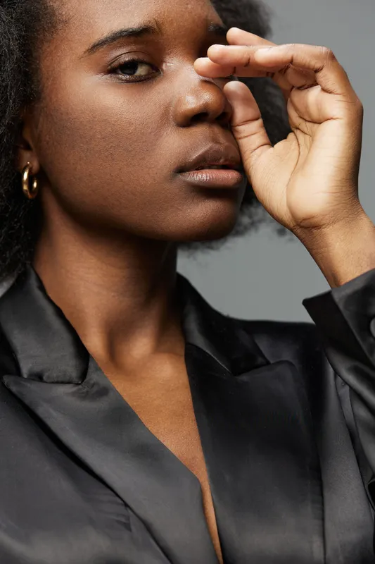 Portrait of a confident African woman in a black satin blouse, showcasing natural beauty and emotions against a soft gray background KEY portrait, woman, confidence, beauty, satin, black, emotional