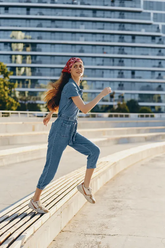 lifestyle woman in modern boho-western denim street style jumping outdoors with casual outfit and red bandana, film color capturing joyful motion and freedom